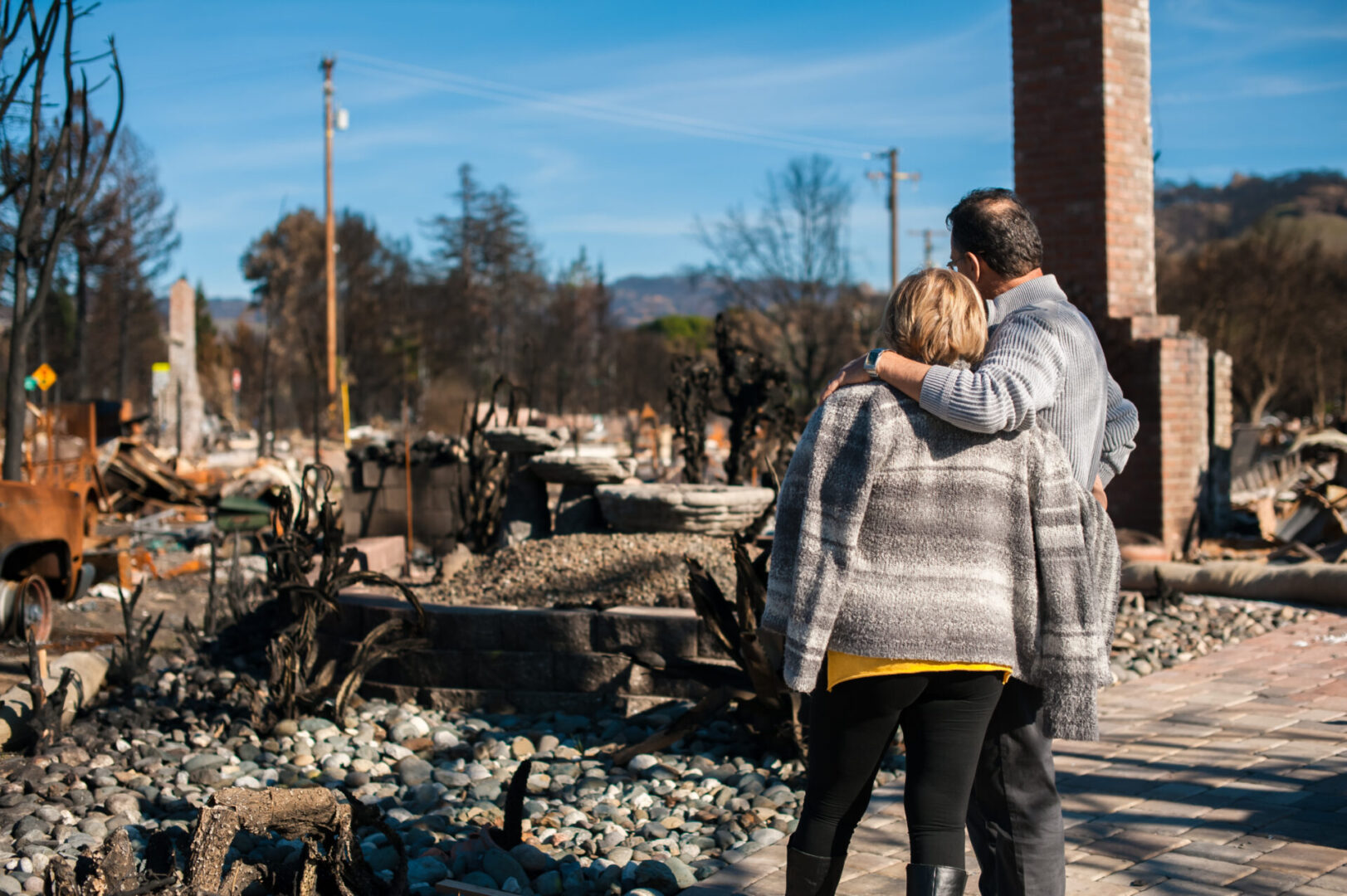 A man and woman hugging in front of a fire damaged building.